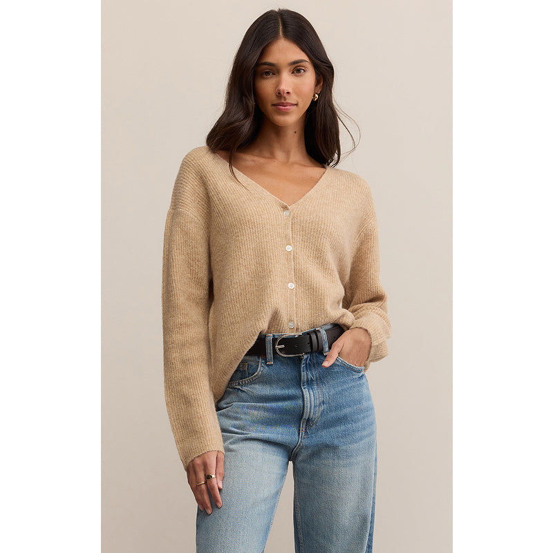 Woman wearing a beige cardigan and blue jeans against a neutral background