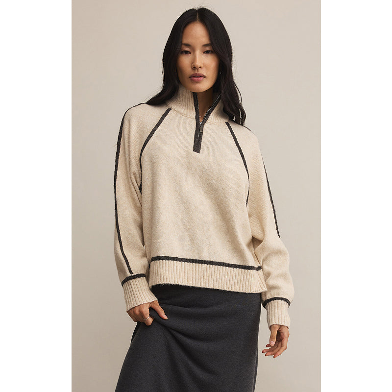 Woman wearing a beige sweater with black accents on a neutral background