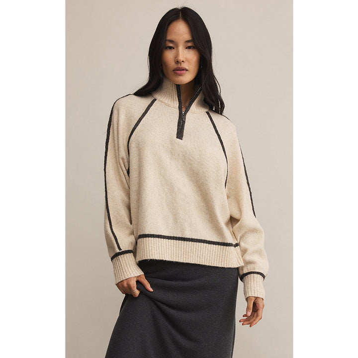 Woman wearing a beige sweater with black accents on a neutral background