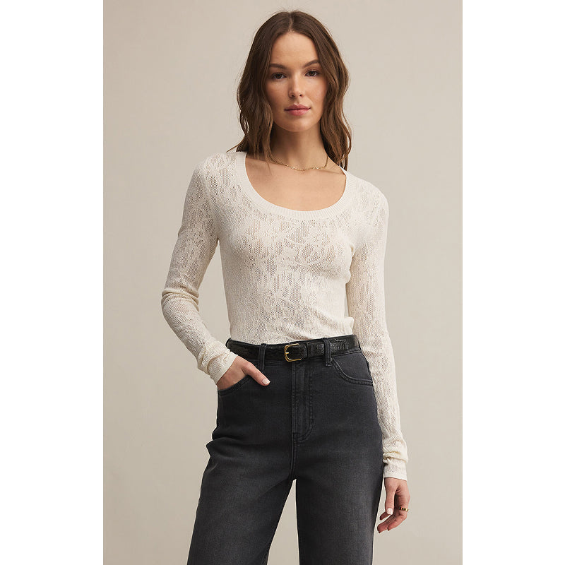 Woman wearing a white lace long-sleeve top and black pants on a neutral background