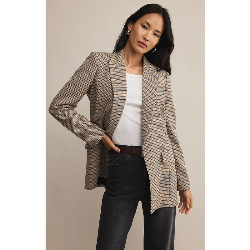 Woman wearing a patterned blazer over a white top and black pants on a beige background