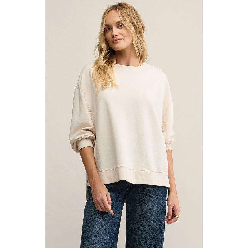 Woman wearing a white sweater and blue jeans against a plain background