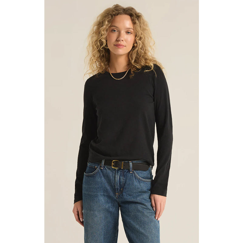 Woman wearing a black long-sleeve top and blue jeans against a beige background