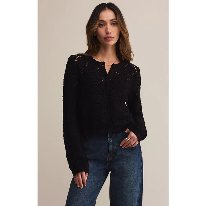 Woman wearing a black lace top and blue jeans against a neutral background